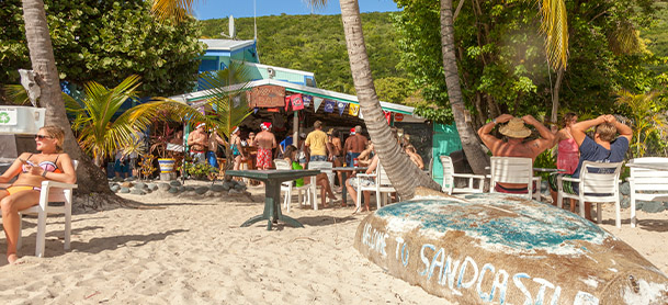 A beach bar in the British Virgin Islands with people in bathing suits standing and holding drinks