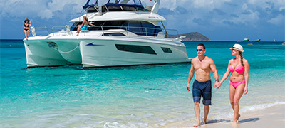 Couple walking on beach with MarineMax Vacations 443 Power Catamaran in background