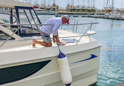 Man installing bumbers to side of boat docked in water