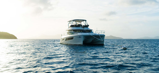 Yacht anchored in blue water with sun shining in the distance