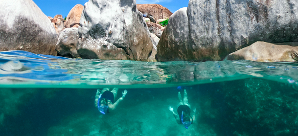 Two people scuba diving underwater with rocks above the surface