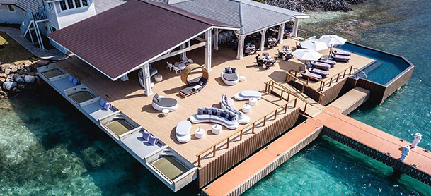 A collection of tables and chairs on a wooden patio next to clear blue-green water