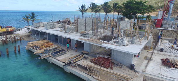 A resort in the British Virgin Islands being reconstructed, with palm trees and blue water in the background