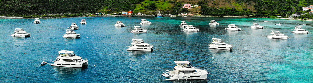 A wide shot of a group of Aquila power catamarans in clear blue-green water off the coast of the British Virgin Islands