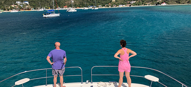 A man and woman standing at the stern of an Aquila power catamaran, looking off at the coastline of the British Virgin Islands