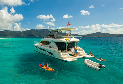 A MarineMax power catamaran idle in clear water with people kayaking, paddleboarding, and snorkeling