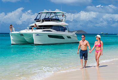 couple walking on beach with power catamran behind them