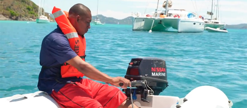 Man in life jacket powering dinghy boat engine