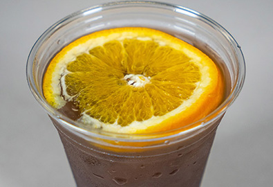 A cocktail in a clear plastic cup with a slice of orange on top