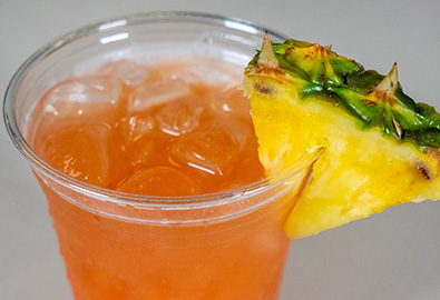 A cocktail in a clear plastic cup with a slice of pineapple on top