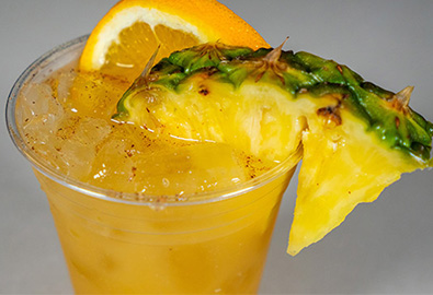 A cocktail in a clear plastic cup with a slice of pineapple and a slice of orange on top