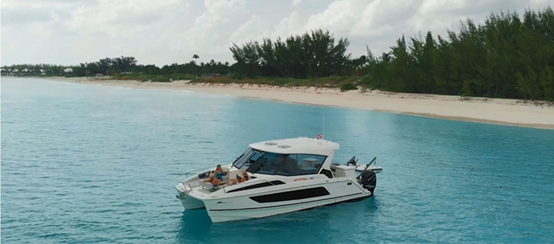 A stationary Aquila power catamaran close to shore in the Abacos, Bahamas surrounded by clear water and white sand