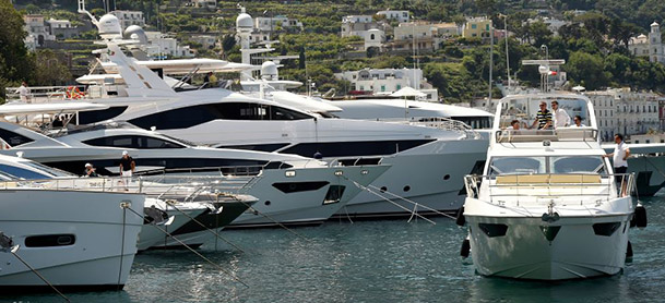 An Azimut yacht cruises by several docked boats in a marina in Italy
