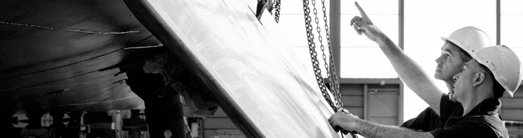 black and white photo of two men standing near a Benetti yacht being built with one of the men pointing up at the yacht