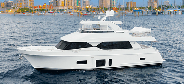 A white Ocean Alexander yacht sails in calm waters with a cityscape in the background, featuring skyscrapers and docked boats.