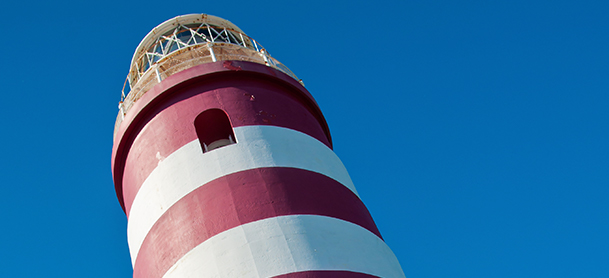 Looking up at a red and white lighthouse on a sunny day