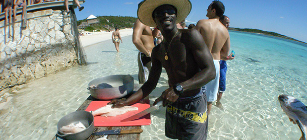 A man stands in front of a table in shallow water while slicing fish