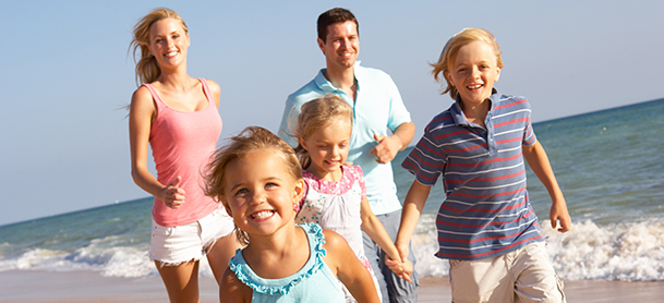 A family walk along a beach while smiling with waves crashing behind them