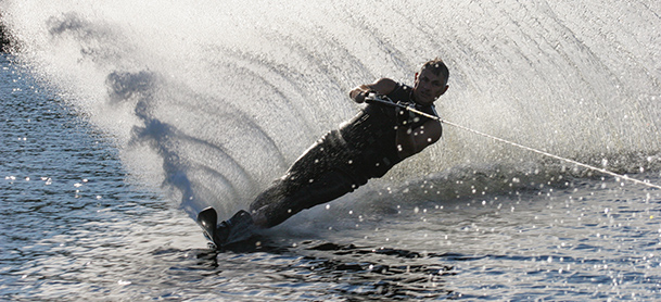 A man waterskis while leaving a big wave behind him