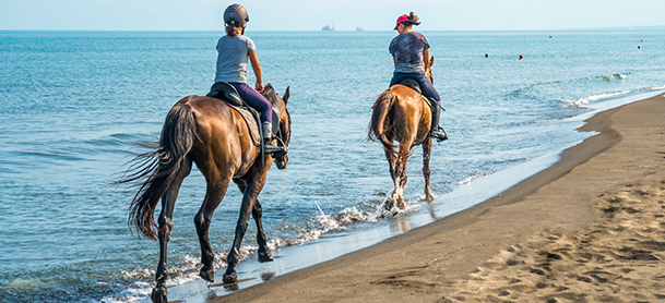 Two women ride horses along a beach