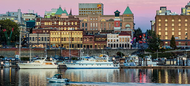 A city skyline lit up in the evening with boats in a marina in the foreground
