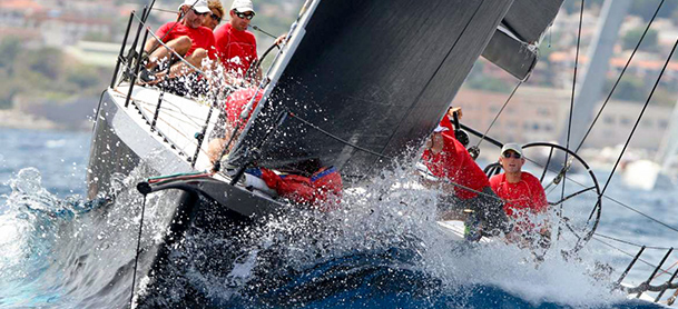 A boat full of people in red shirts rocks to the side while being hit by a wave