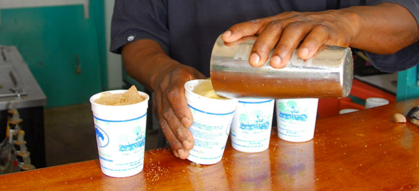 A row of white cups being filled with a beverage from a large glass