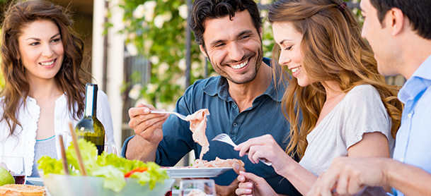 Two men and two women eat at a dinner table with platters of food in front of them