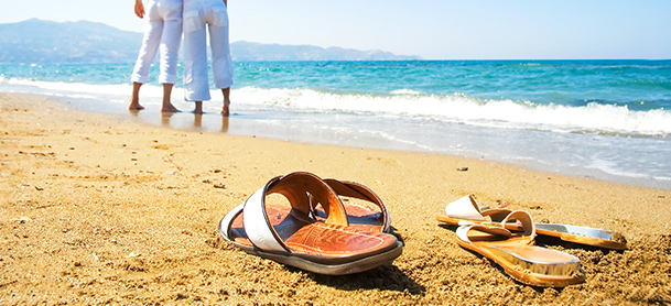 Sandals left on beach as people in white pants walk along beach