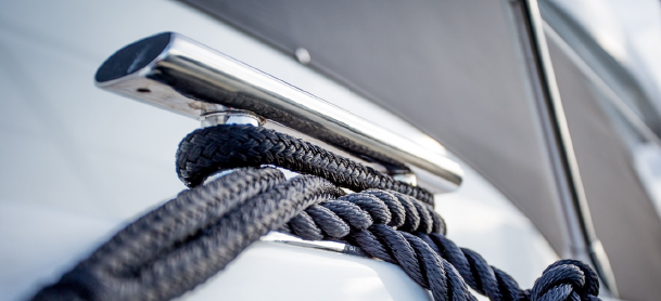 A close-up of a shiny metal cleat on a boat, with thick black ropes neatly coiled around it.