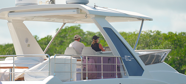 Two people test drive a yacht under a canopy, enjoying a sunny day.