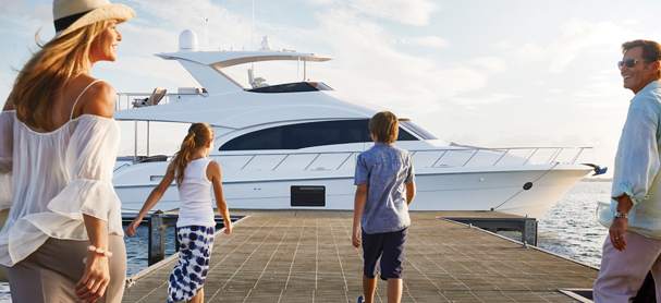 A mother and father with two young kids walk along a dock toward a yacht
