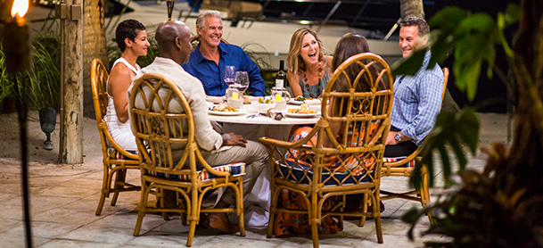 group of people sitting at a table eating dinner with a boat along the dock in the background