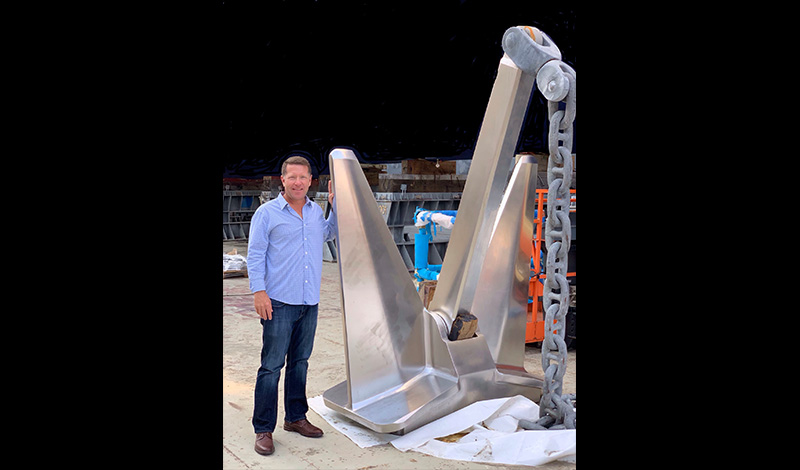 a yacht salesman standing in a boat factory next to a large piece of metal