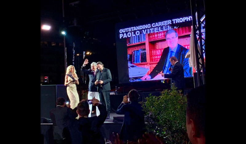 a man accepting an award at a yacht awards show for outstanding career with a photo of him in the background