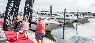 people walking down dock on red carpet with MarineMax Yachts flags flying as yachts are lined up