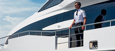 man in uniform standing on side deck of yacht