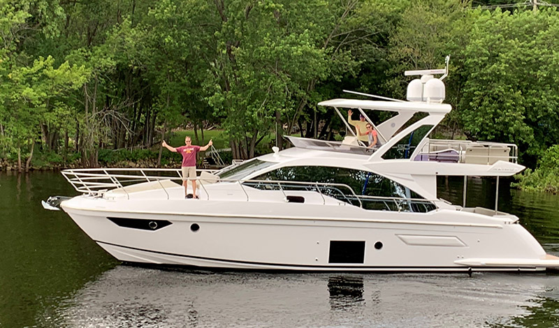 a profile view of an azimut 50 flybridge with three people aboard and trees in the background
