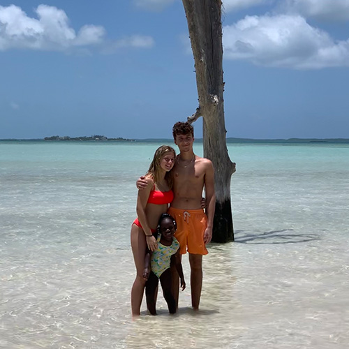 three kids standing in shallow water with a tall tree behind them