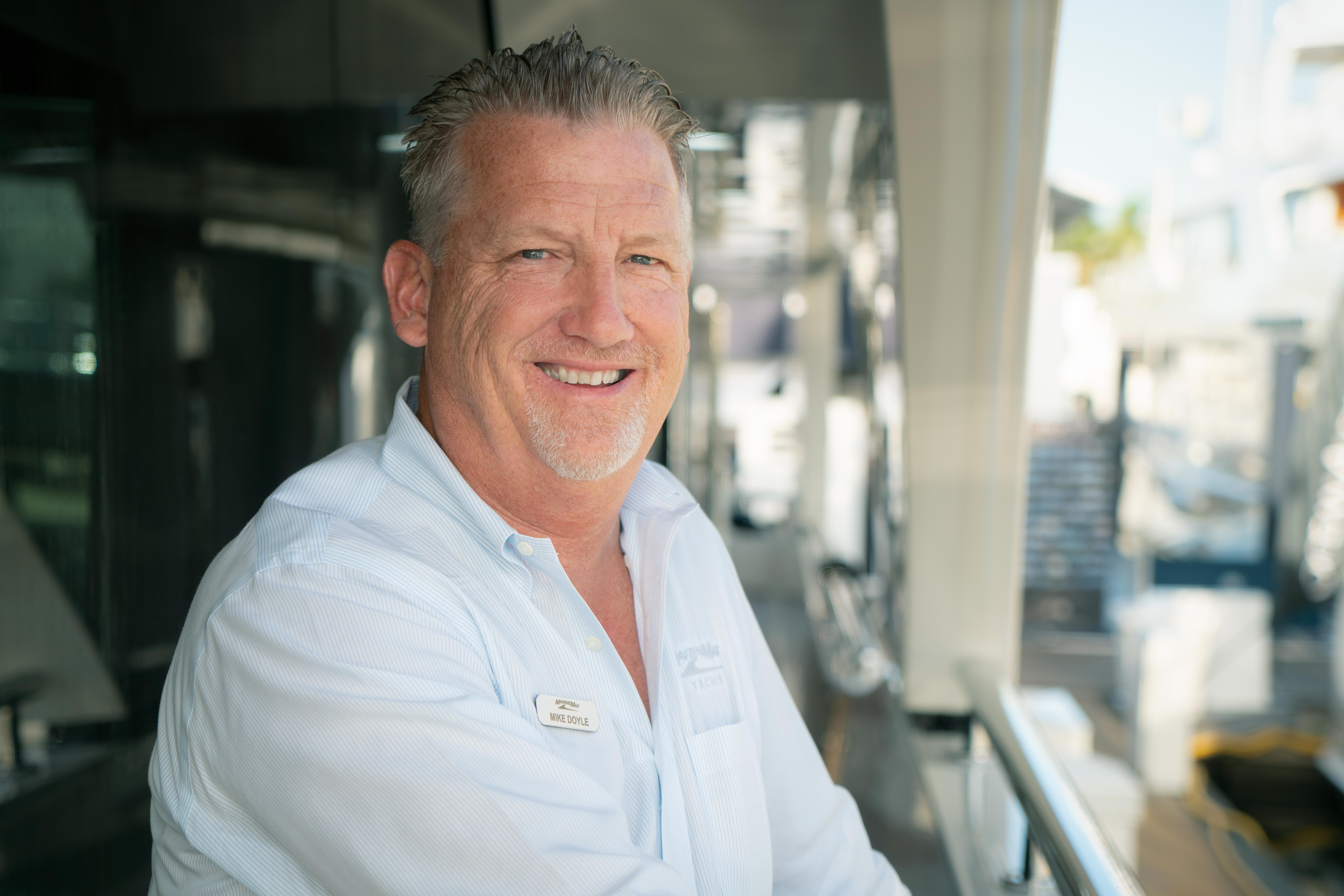 a man in a button down shirt smiles while standing at a marina