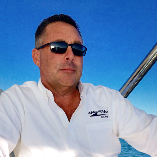 a man in sunglasses and a white polo looks off the stern of a boat