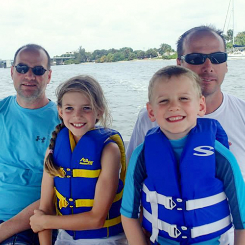 two men sit on a boat with two children in life jackets in front of them