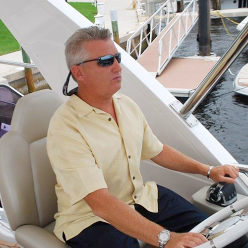 a man in sunglasses sits at the helm of a boat