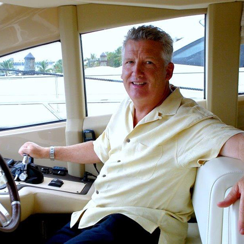 a man sits smiling at the helm of a boat