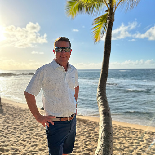 scott roberton next to a palm tree on the beach